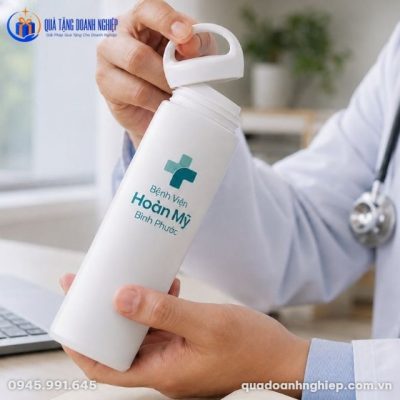 Cận cảnh thao tác vặn mở nắp bình giữ nhiệt in logo Hoàn Mỹ bằng quai xách tiện lợi trong không gian làm việc y tế