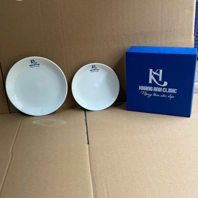 Bộ sản phẩm đĩa sứ trắng thực tế đặt cạnh hộp quà cứng cáp màu xanh dương trên nền carton
