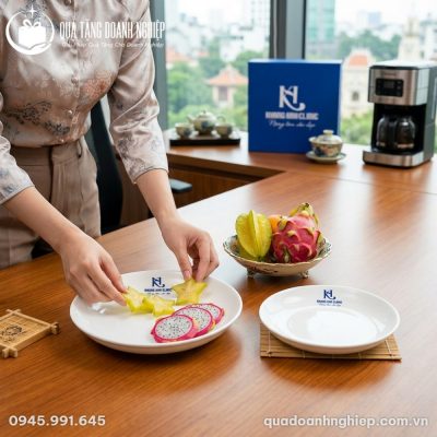 Đôi bàn tay thanh lịch của nữ nhân viên công sở nâng niu chiếc đĩa sứ trắng in logo sắc nét