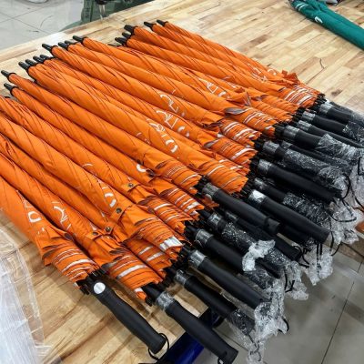 Hàng loạt ô dù gấp gọn màu cam được bọc nilon bảo vệ phần tay cầm xếp gọn gàng trên bàn gỗ