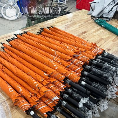 Hàng loạt ô dù gấp gọn màu cam được bọc nilon bảo vệ phần tay cầm xếp gọn gàng trên bàn gỗ