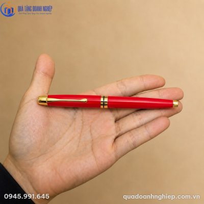 Cận cảnh chiếc bút ký kim loại màu đỏ mạ vàng đặt ngang trên lòng bàn tay thể hiện kích thước cân đối