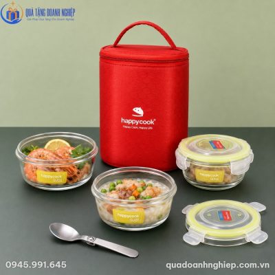 Bộ ba hộp thủy tinh tròn chứa tôm luộc, cháo thịt bằm đậu hà lan và một hộp đậy nắp bên cạnh chiếc muỗng inox gấp gọn và túi giữ nhiệt màu đỏ phía sau