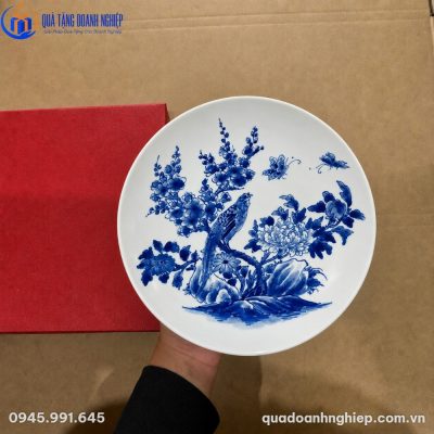 Cận cảnh đĩa biểu trưng sứ trắng vẽ tay hoa mẫu đơn và chim trĩ đặt cạnh hộp đựng màu đỏ