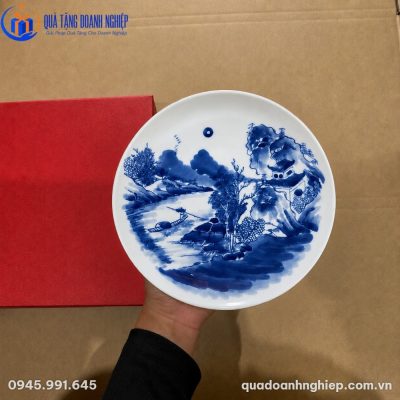 Đĩa biểu trưng sứ vẽ tay chi tiết sơn thủy men lam đặt cạnh hộp xi đỏ sang trọng