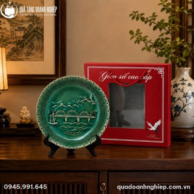 Đĩa sứ biểu trưng BDT-04 đặt cạnh hộp đựng lót lụa màu đỏ sang trọng trên bàn gỗ cổ kính