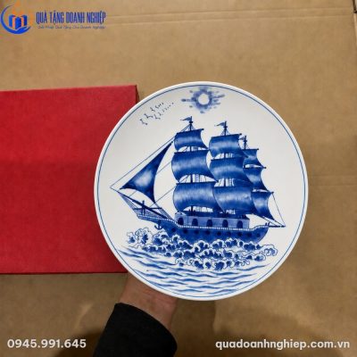 Cận cảnh đĩa biểu trưng sứ trắng vẽ tay Thuận Buồm Xuôi Gió cùng hộp đựng màu đỏ sang trọng trên tay người sử dụng