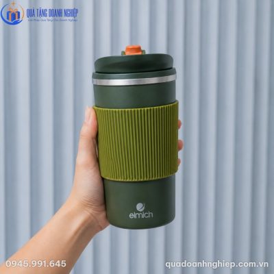 Cận cảnh bàn tay đang cầm chiếc ly giữ nhiệt Elmich màu xanh lá nổi bật với phần đệm silicon gợn sóng màu xanh cốm