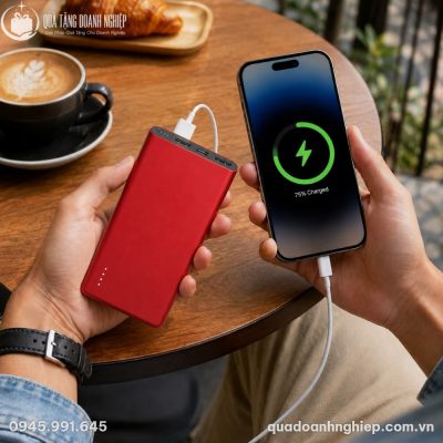 Người dùng cầm trên tay sạc dự phòng Akus Vivu V10 màu đỏ và điện thoại khi đang làm việc tại quán cà phê