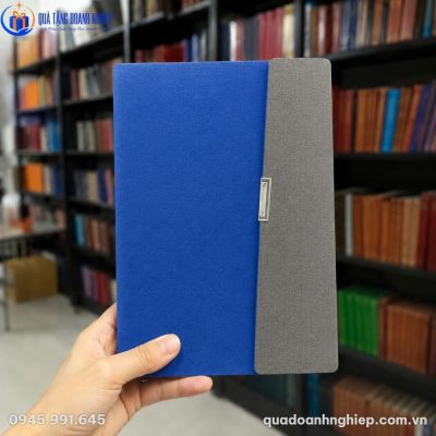 Cận cảnh cuốn sổ còng SD-10 màu xanh coban phối xám ghi trên tay người dùng trong không gian thư viện