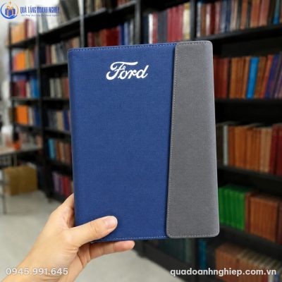 Cận cảnh cuốn sổ da phối màu xanh xám in logo Ford màu trắng sắc nét được cầm trên tay tại thư viện
