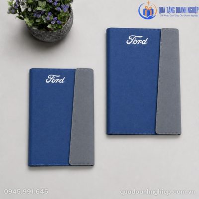 Hai cuốn sổ da A5 in logo Ford đặt song song trên mặt bàn phẳng cạnh chậu cây nhỏ góc nhìn từ trên xuống
