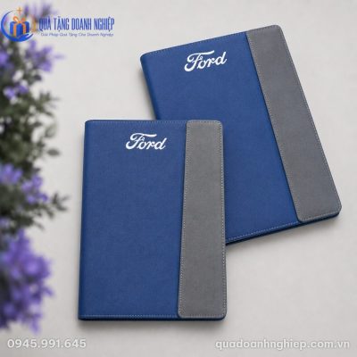 Góc chụp nghiêng hai cuốn sổ da phối màu hiện đại xếp chồng nhẹ lên nhau cạnh khóm hoa tím