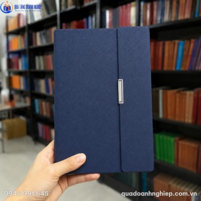 Cận cảnh cuốn sổ da PU vân cát mịn màu xanh navy trên tay người dùng với khóa cài kim loại sang trọng