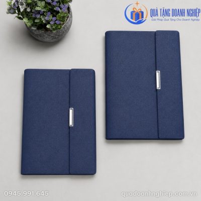 Hai cuốn sổ còng 3 khúc thẳng A5 in logo quà tặng SD-11 đặt song song trên mặt bàn phẳng cạnh chậu cây