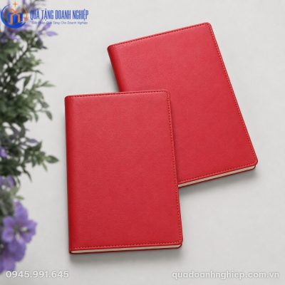 Góc chụp nghiêng hai cuốn sổ da màu đỏ xếp chồng lên nhau bên cạnh nhành hoa tím