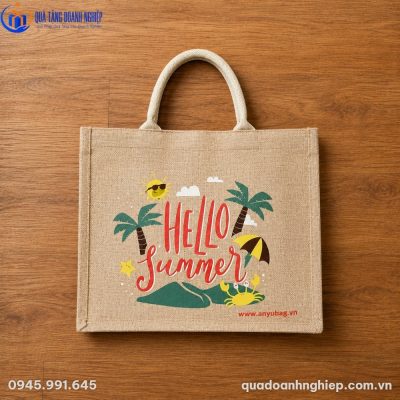 Mặt trước túi canvas cói TVQT-11 đặt phẳng trên nền sàn gỗ, thể hiện rõ bề mặt vải đay dệt thô mộc mạc và họa tiết in sắc nét