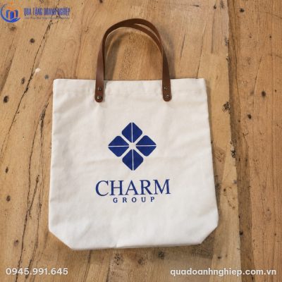 Mẫu túi tote canvas CVQT-01 thực tế đặt trên mặt bàn gỗ với quai da PU màu nâu bò cùng đinh tán kim loại chắc chắn