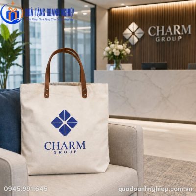 Túi tote canvas in logo thương hiệu Charm Group sắc nét đặt trên ghế sofa tại khu vực sảnh đón khách sang trọng