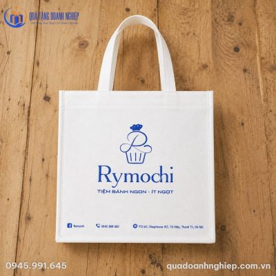 Túi vải không dệt KDQT-02 in logo xanh cobalt nổi bật trải phẳng trên nền sàn gỗ tự nhiên
