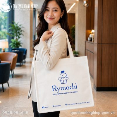 Người mẫu công sở Việt Nam đeo chiếc túi vải không dệt phom dáng vuông vắn phối logo Rymochi xanh