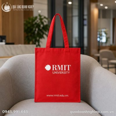 Thiết kế mặt trước túi vải canvas đỏ RMIT đặt trên ghế sofa tối giản trong không gian văn phòng