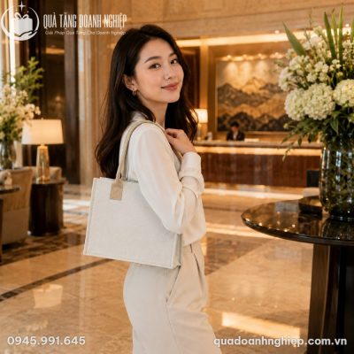 Nữ nhân viên công sở thanh lịch phối đồ tông kem trang nhã khoác chiếc túi vải canvas dệt chất lượng cao tại sảnh khách sạn 5 sao.