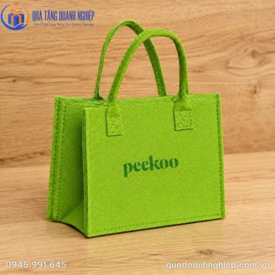 Chi tiết chất liệu nỉ felt dày dặn và đường may tỉ mỉ của túi nỉ xanh lá khi đặt trên mặt gỗ.
