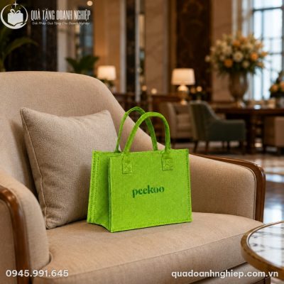 Túi nỉ xanh lá in logo đặt hài hòa trên ghế sofa phòng chờ hiện đại.